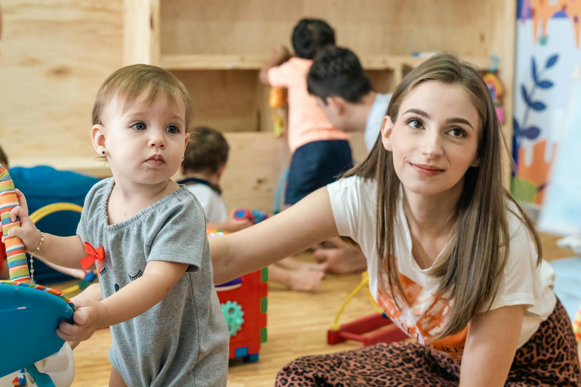 A joyful mother and her baby girl playing together in a vibrant indoor nursery setting.