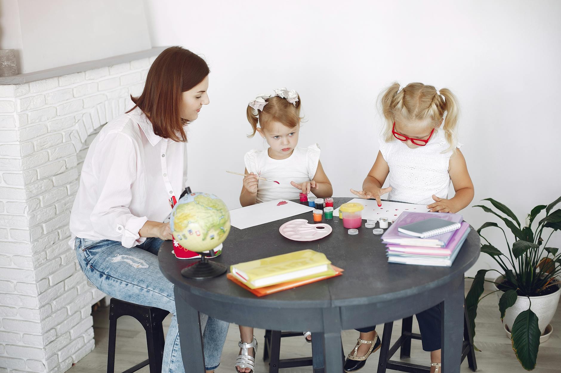 Small kids attentively painting in kindergarten with adult assistance while sitting together at round table