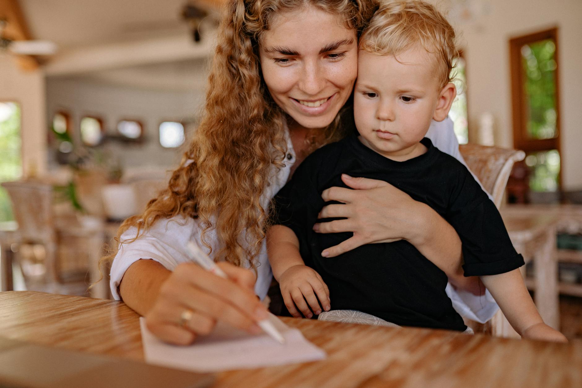 Mother holding her young child while writing, creating a bonding moment indoors.