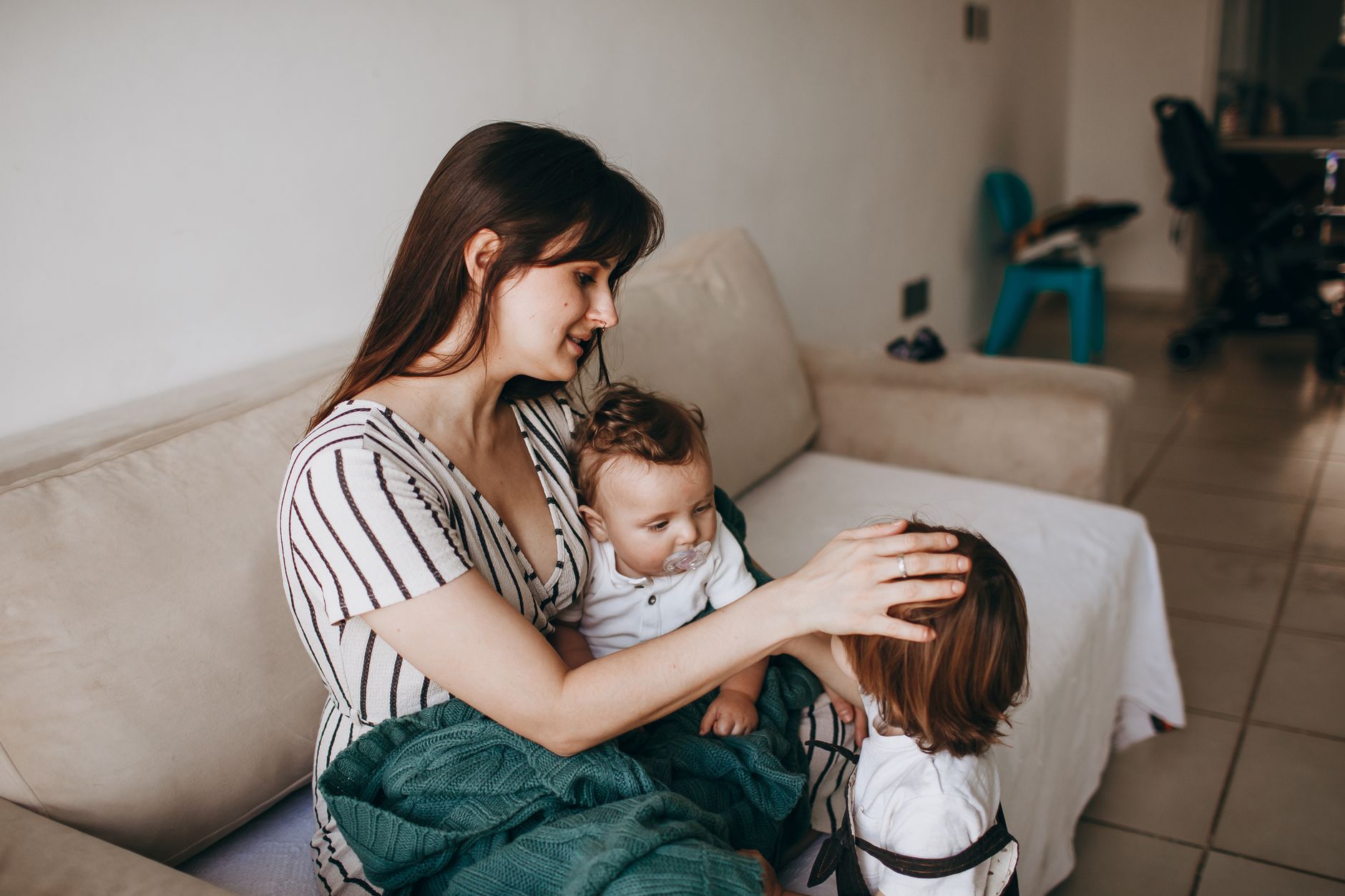 A mother lovingly cares for her two young children in a cozy home environment, creating a warm family moment.