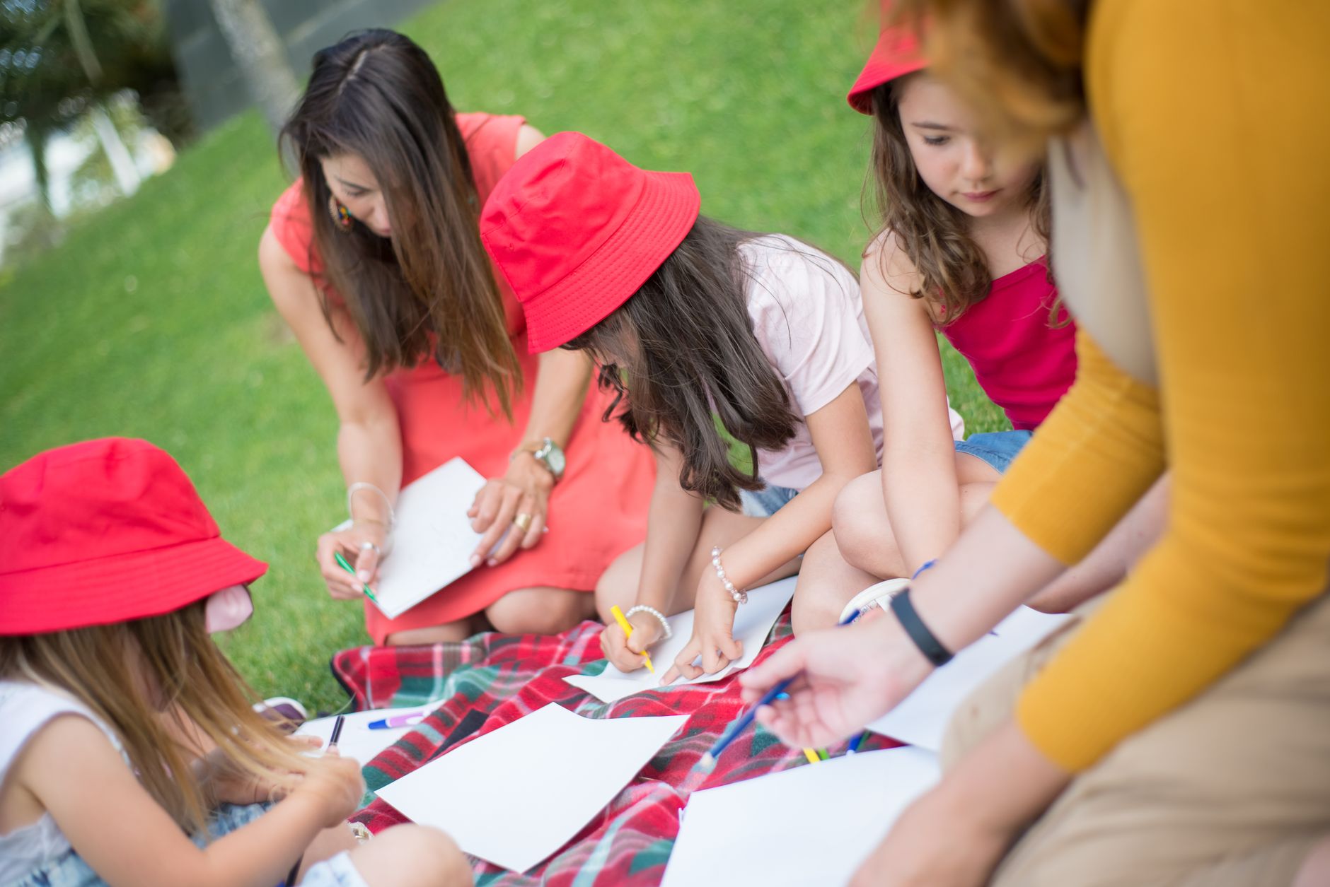 Children and nanny enjoying an outdoor drawing session in a sunny park.