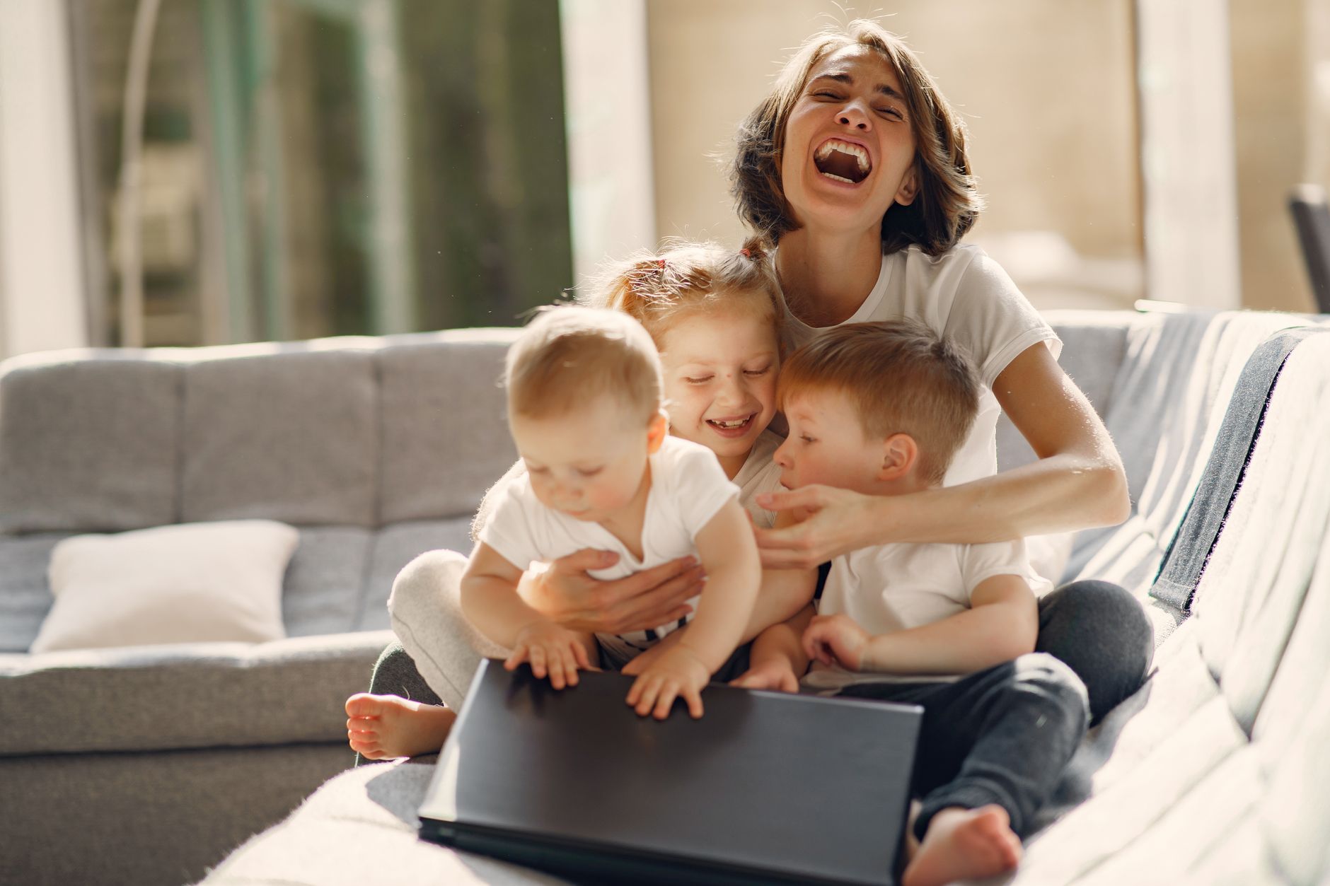 Happy woman laughing and hugging children while sitting on sofa in well lit living room