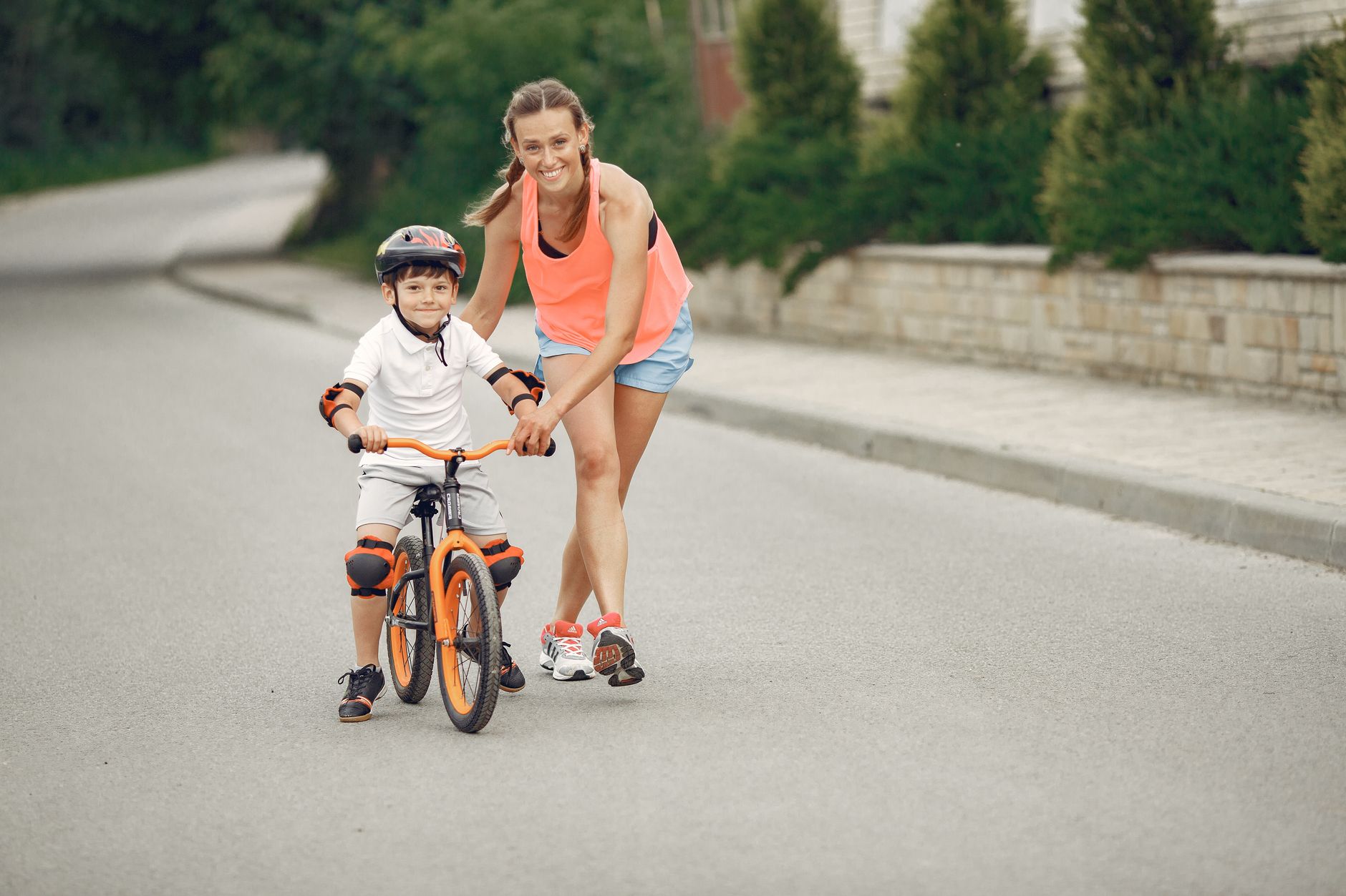 A mother helps her child learn to cycle on a quiet road. Perfect for topics on parenting and outdoor activities.