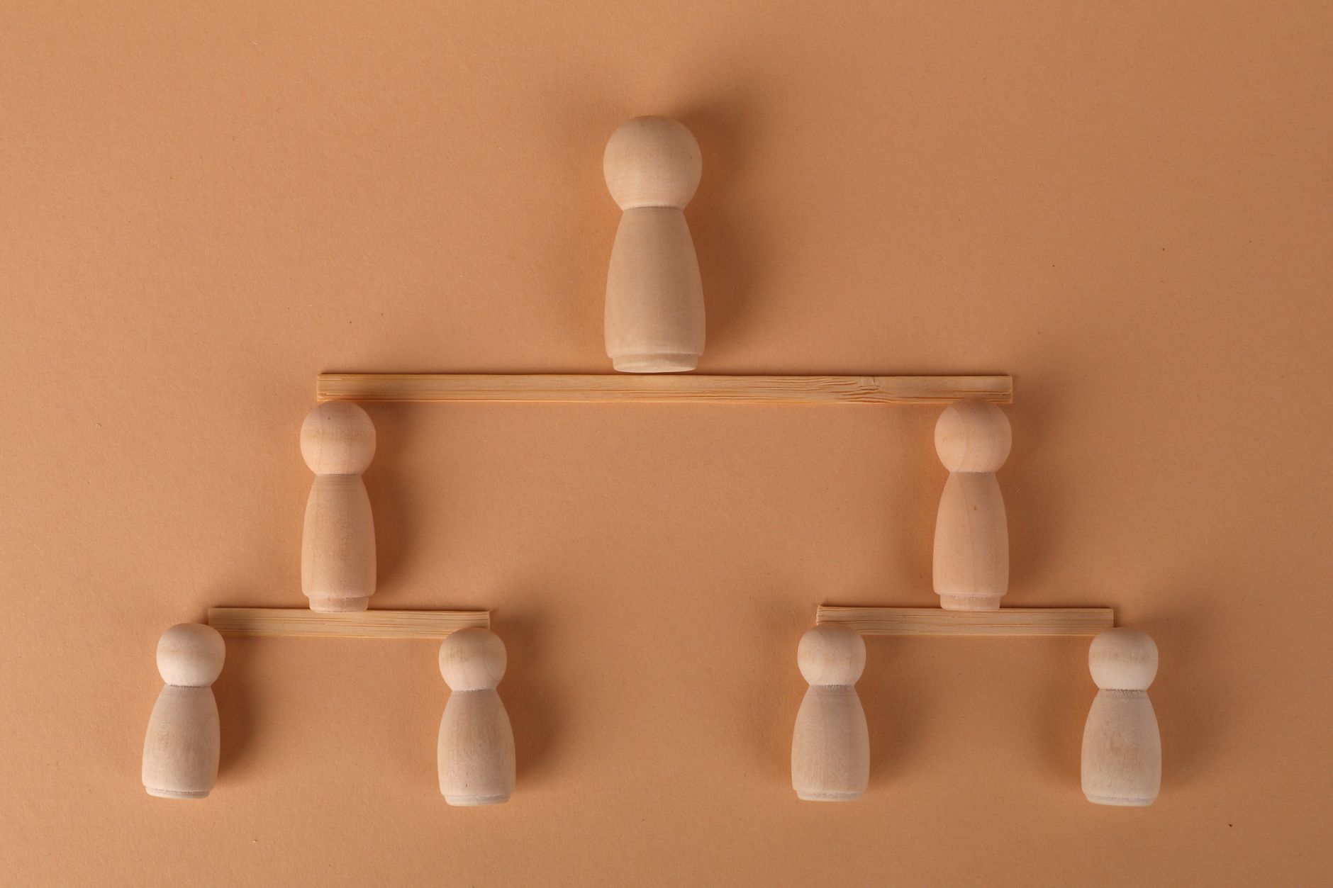Wooden peg dolls arranged to symbolize a hierarchy on a neutral brown background.
